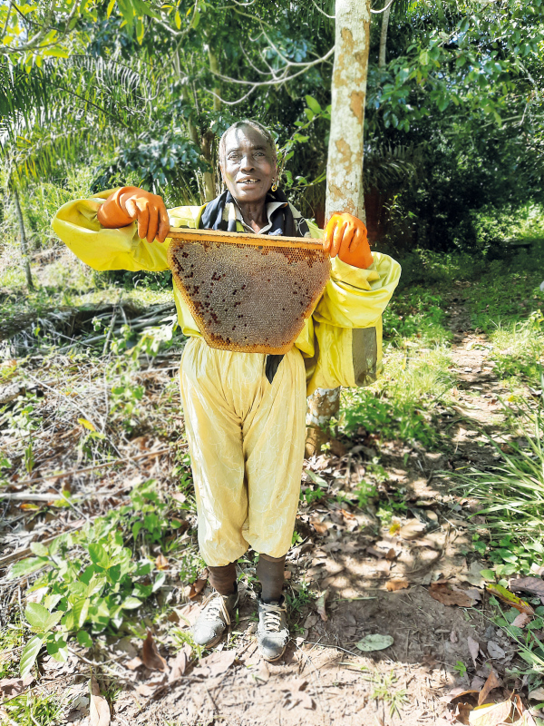Eine Frau aus Kamerun im Imkerschutzanzug hält eine Bienenwabe in die Kamera