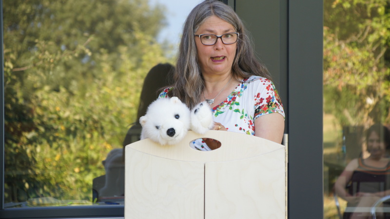 Eine Referentin steht mit einem Eisbären-Stofftier hinter einem Holztheater und startet eine Geschichte.