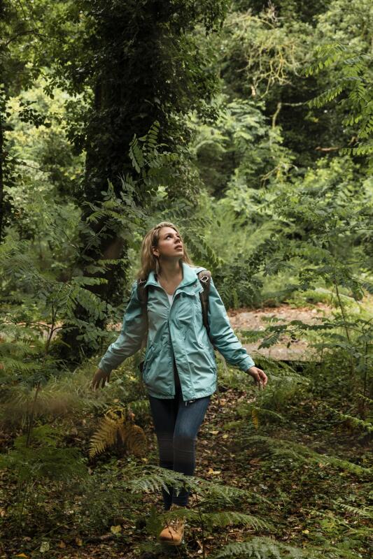 Eine junge Frau in Funktionskleidung geht staunend durch einen Wald
