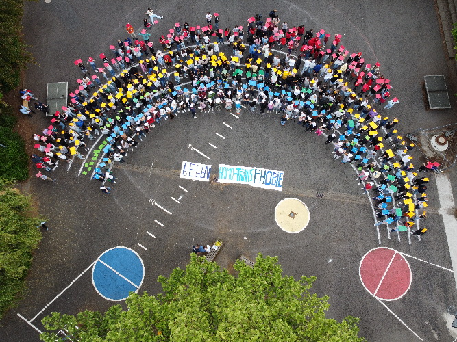 Schülerinnen und Schüler der Mathilde-Anneke-Gesamtschule bilden im Sinne eines Regenbogens einen farbenfrohen Halbkreis rund um den Spruch „Gegen Trans-/Homophobie“
