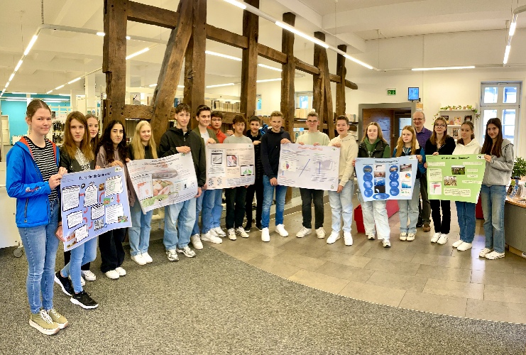 Das Bild zeigt die Schülerinnen und Schüler des Umwelt-Kurses mit ihren Plakaten zur klimafreundlichen Ernährung, die in der Stadtbücherei Rietberg ausgestellt wurden.