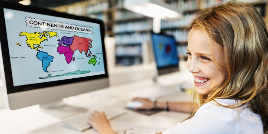 Mädchen sitzt lächelnd vor einer bunten Weltkarte auf dem PC