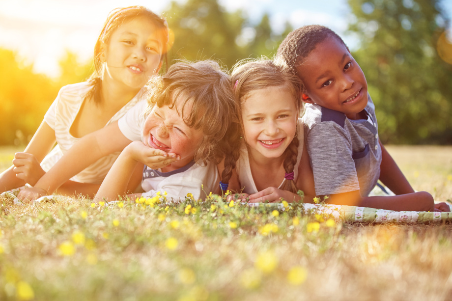 Vier Kinder liegen bäuchlings auf einer Sommerwiese und lächeln in die Kamera