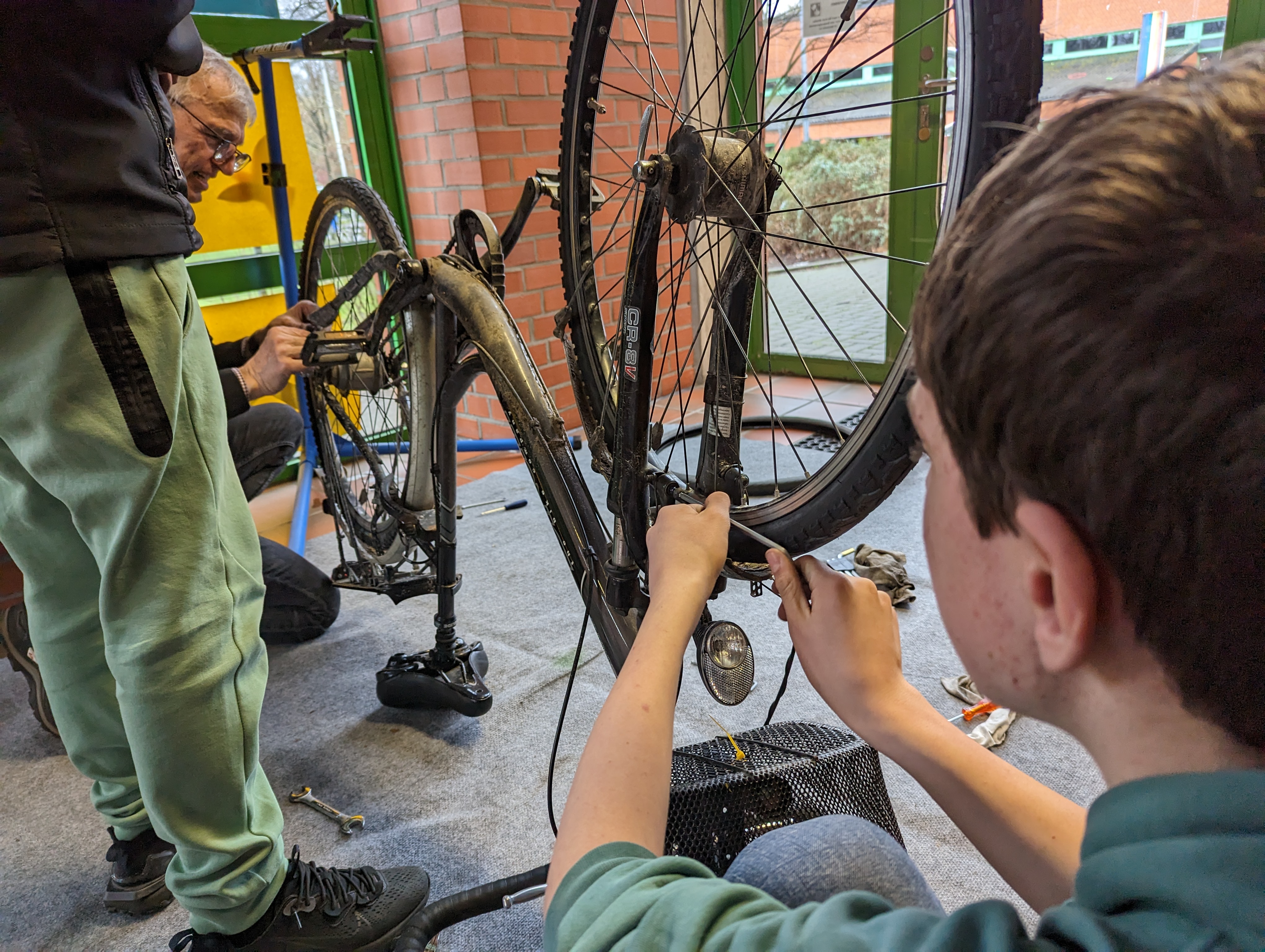 Zwei Schüler und ein ehrenamtlicher Mitarbeiter reparieren ein Fahrrad