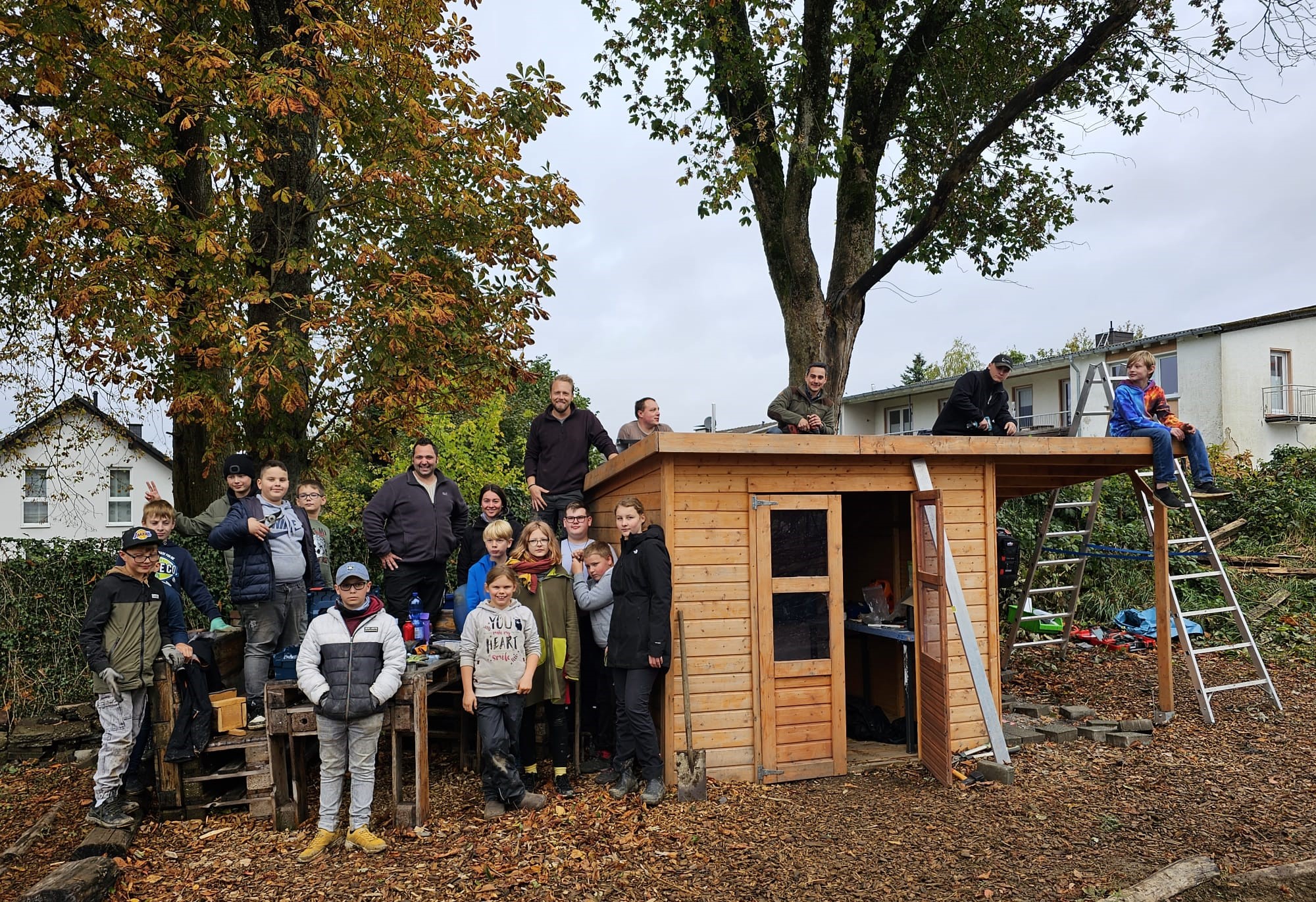 Mehrere Schülerinnen und Schüler, ein Handwerker, eine Lehrerin und zwei Lehrer stehen vor dem Gartenhäuschen im Schulgarten der Gesamtschule Kierspe und freuen sich über die neue Photovoltaikanlage. 
