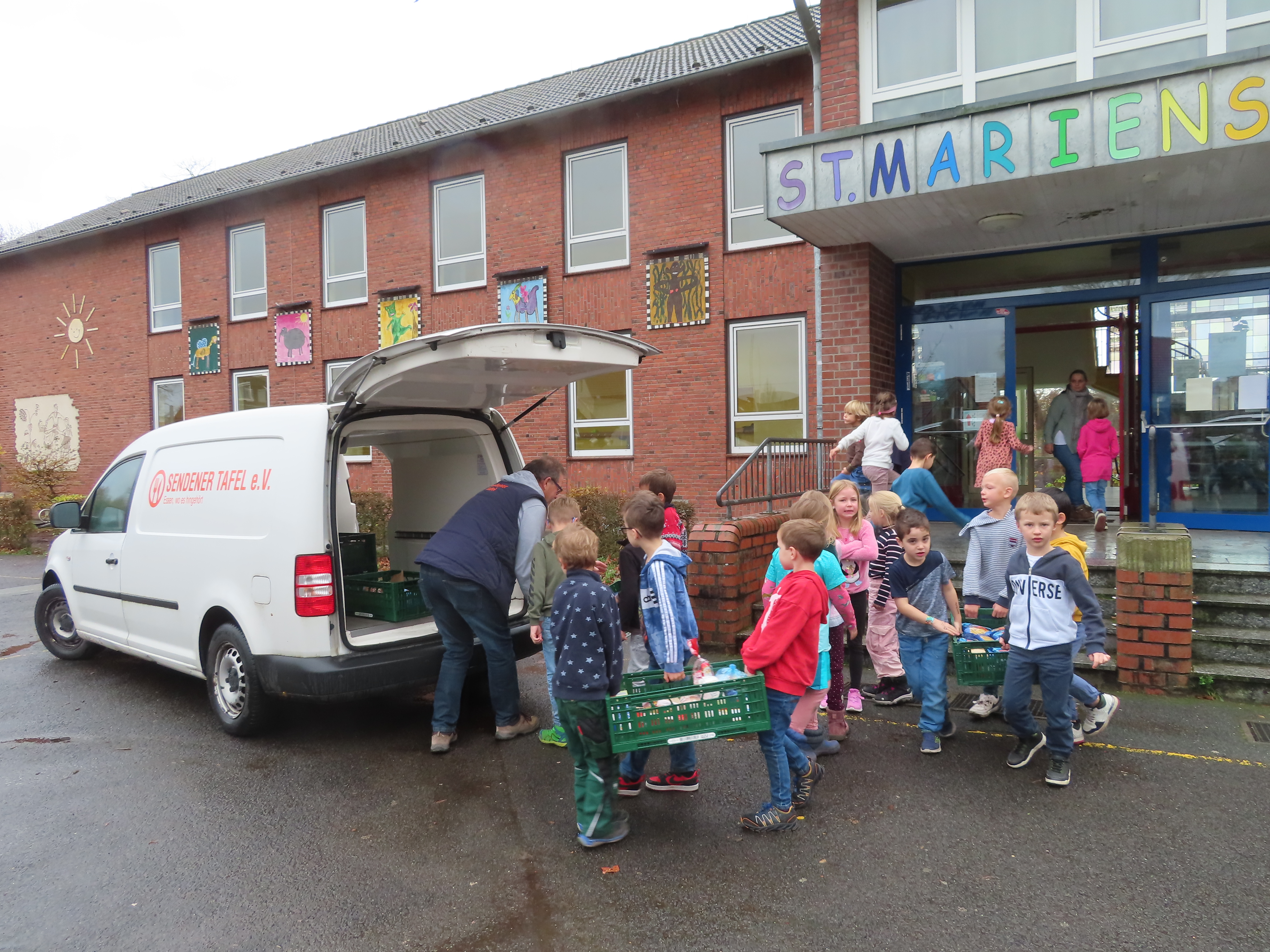 Die Kinder der Klasse 1a laden mit dem Mitarbeiter der Sendener Tafel die gesammelten Spenden in das Fahrzeug.