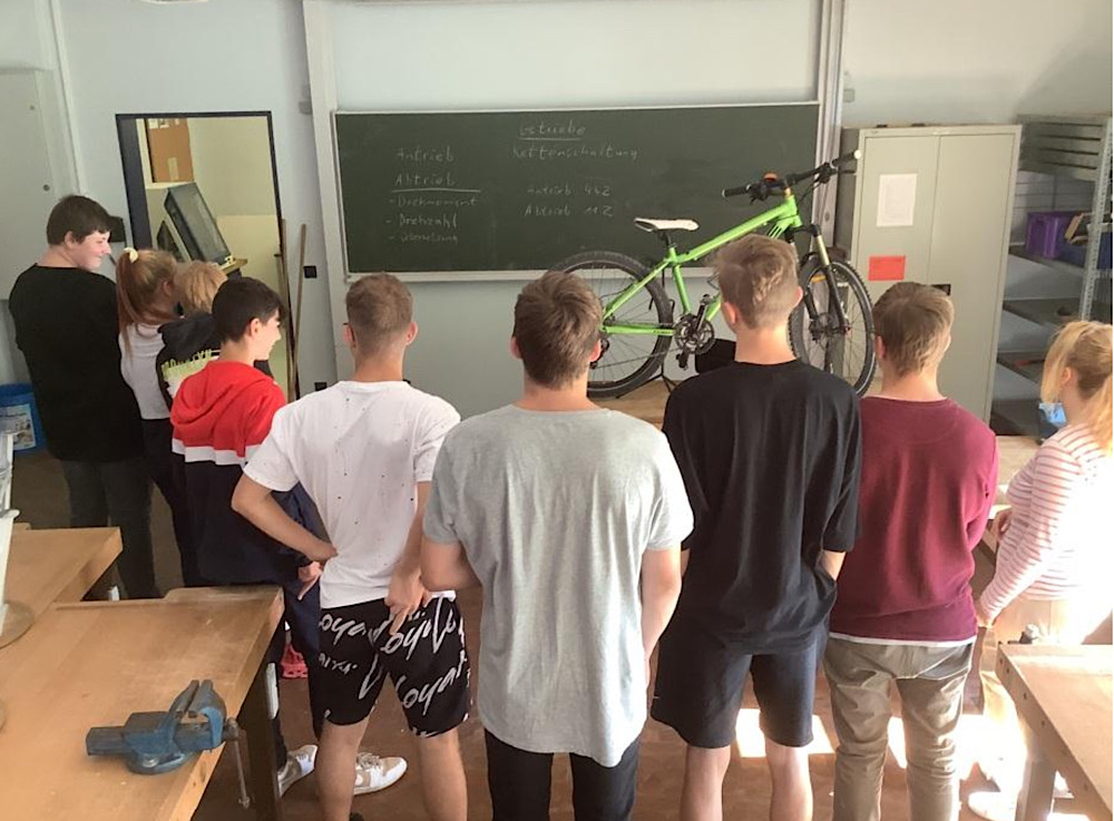Schülerinnen und Schüler begutachten in der Fahrradwerkstatt ein Fahrrad