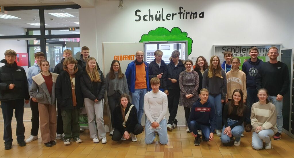 Das Foto zeigt ein Gruppenbild aller Beteiligter vor dem Verkaufstand der Schüler:innen-Genossenschaft “SchereSteinPapier eSG” am Freiherr-vom-Stein-Gymnasium Bünde