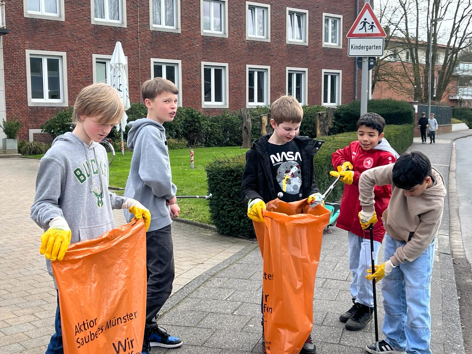 Schüler einer 5. Klasse befüllen einen orangenen Müllsack