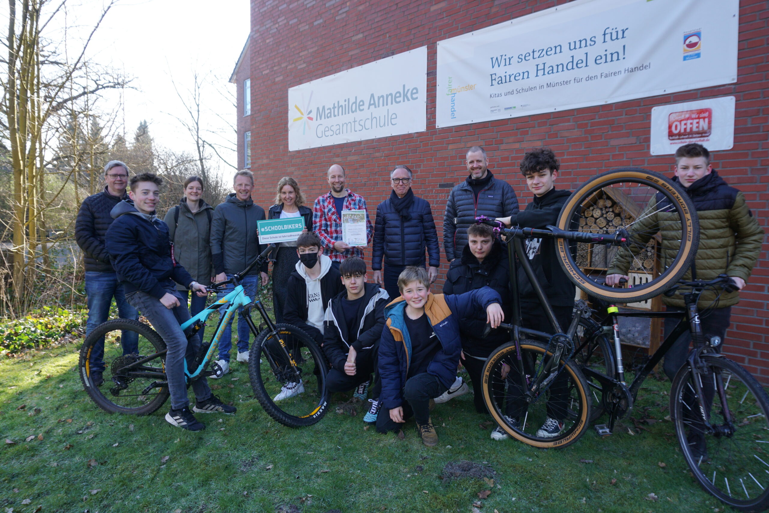 Schüler mit ihren Fahrrädern vor dem Schulgebäude der Mathilde Anneke Gesamtschule, dahinter die Schulleiterin und weitere Lehrer beziehungsweise Erwachsene