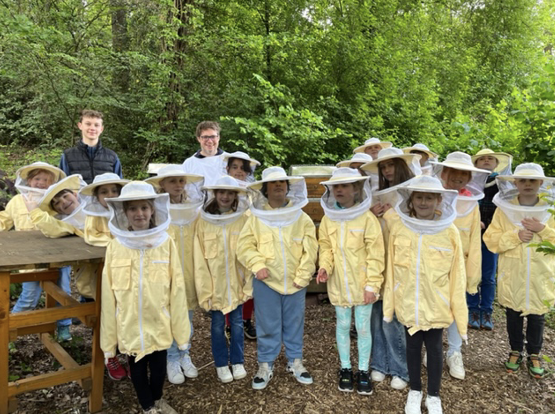Grundschülerinnen und Grundschüler stehen in Imkerausstattung vor zwei Bienenstöcken.