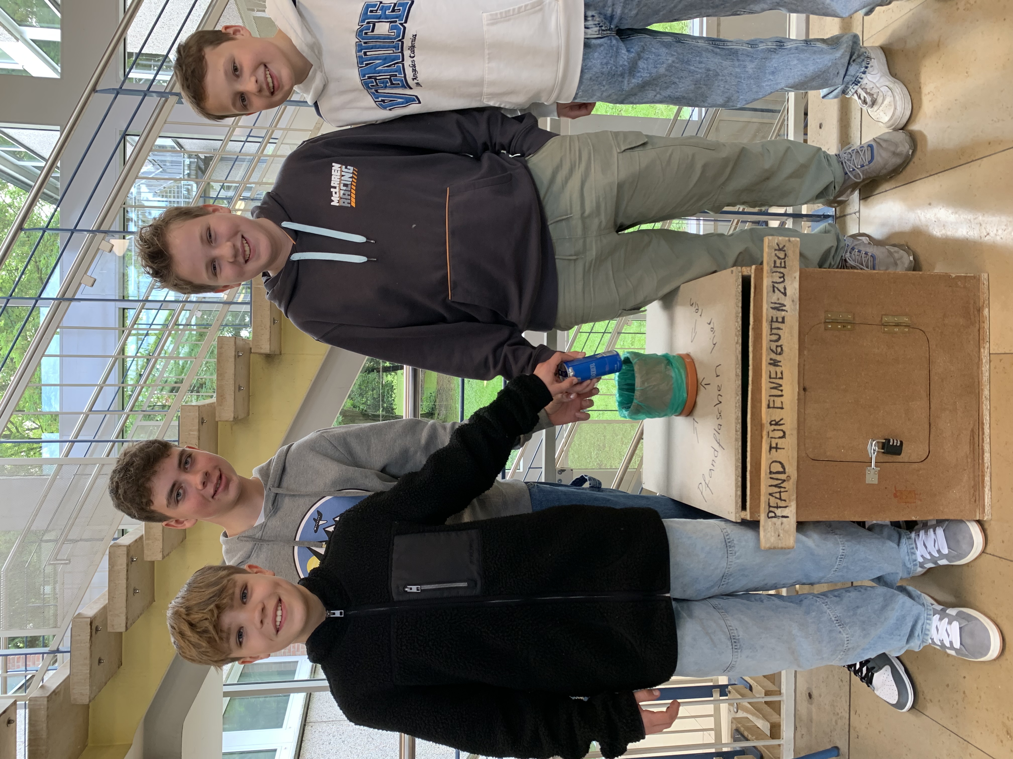 Auf dem Bild sind vier Schüler und eine Pfandflaschensammelbox aus Holz.