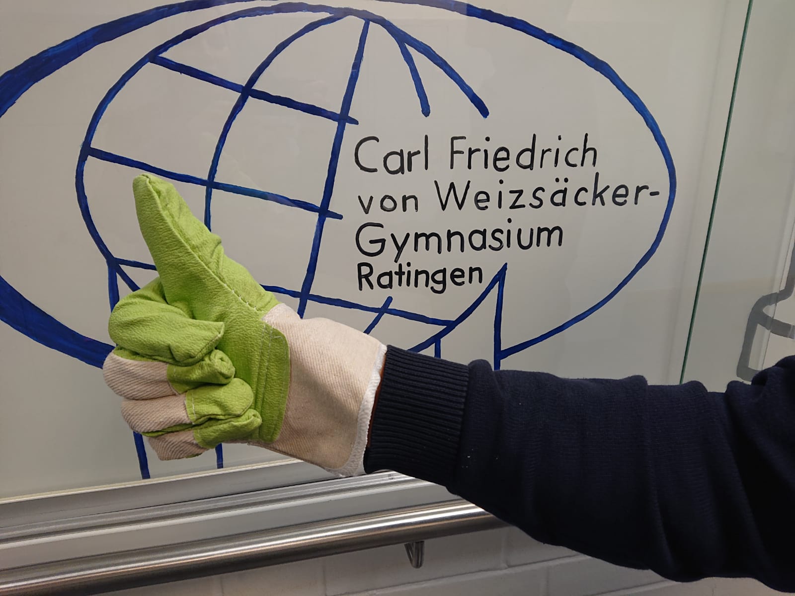 Man sieht einen Handschuh des Dreck-Weg-Tags in Ratingen vor dem Schullogo des CFvW-Gymnasiums.