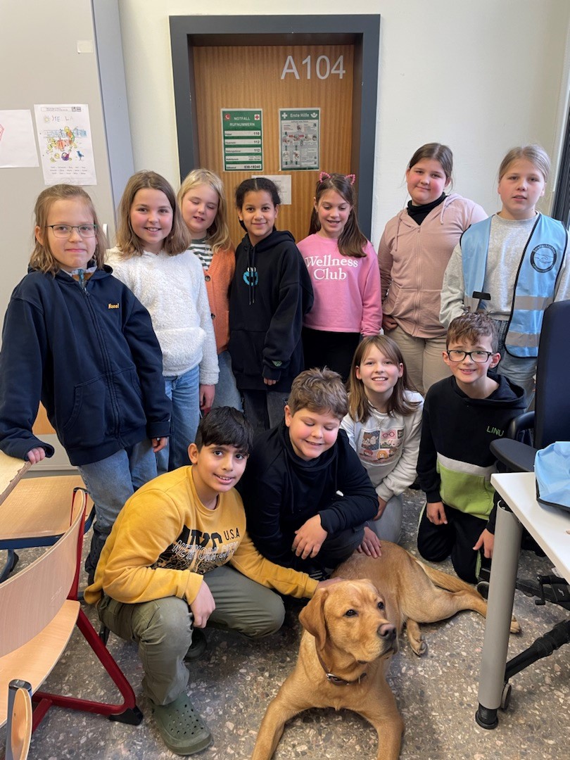 11 stolze Kinder stehen im Halbkreis um den braunen Schulhund Eddi herum