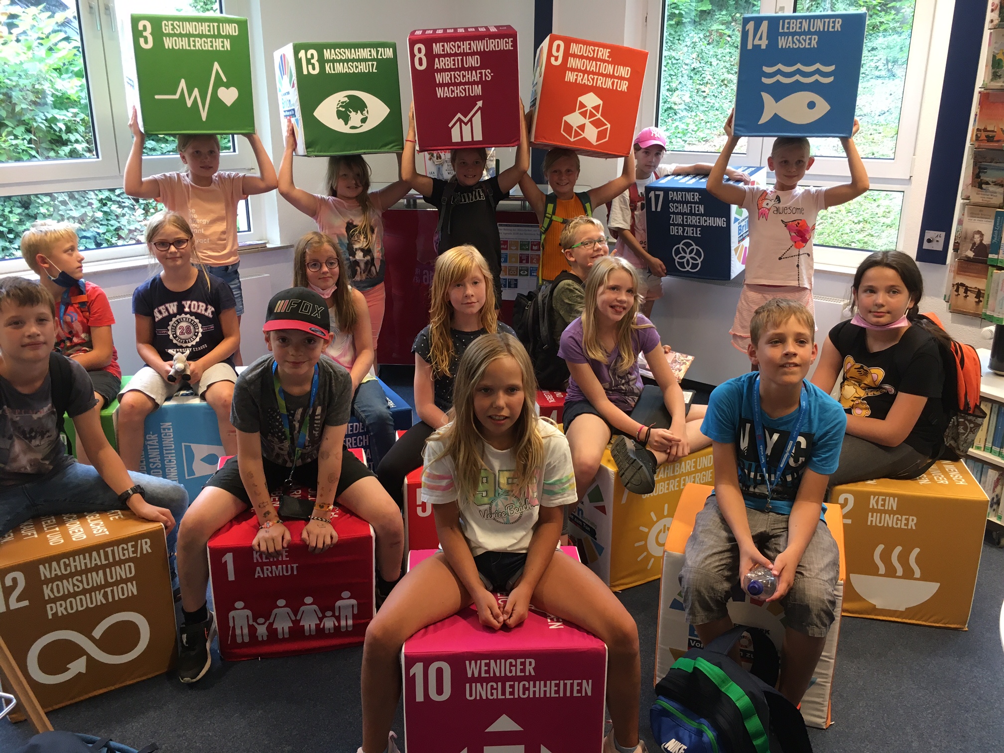 Die Kinder sitzen auf Würfeln oder halten Würfel mit den 17 SDGs.