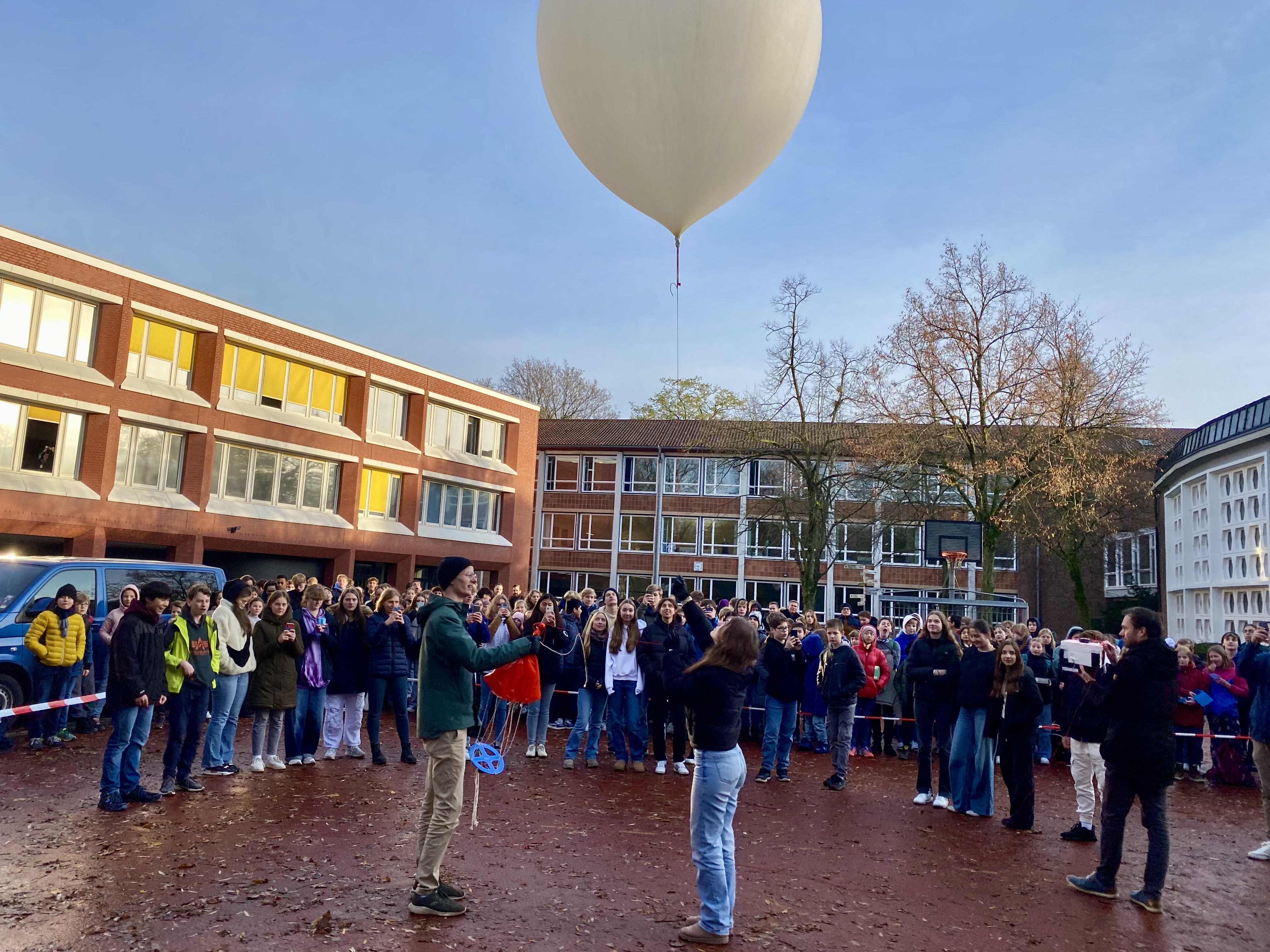 Schülerinnen und Schüler stehen kurz vor dem Start um den Ballon mit der daran hängenden Experimentbox auf dem Schulhof